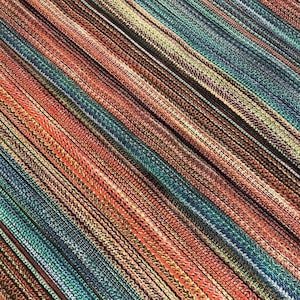 May include: Close-up of a fabric with a diagonal striped pattern. The fabric features a mix of colors, including red, teal, brown, and beige. The stripes are created by woven threads, giving the fabric a textured appearance.