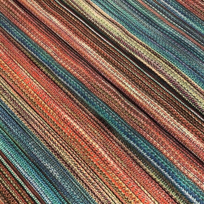 May include: Close-up of a fabric with a diagonal striped pattern. The fabric features a mix of colors, including red, teal, brown, and beige. The stripes are created by woven threads, giving the fabric a textured appearance.