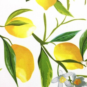 May include: A white background with a yellow lemon pattern. The lemons are on green branches with green leaves. There are also white flowers with yellow centers.
