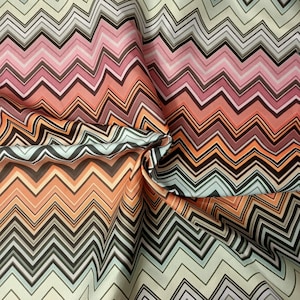 Op de afbeelding: Een stof met een chevron-patroon in tinten oranje, roze, bruin en wit.