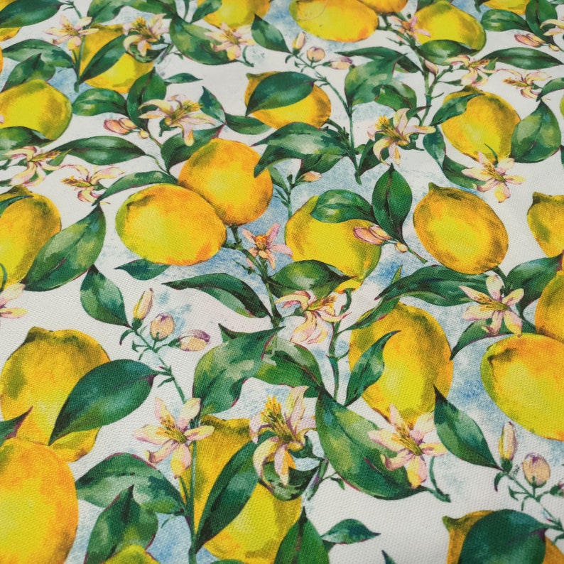 May include: A white fabric with a repeating pattern of yellow lemons and green leaves. The lemons are painted in a watercolor style and have a realistic appearance.