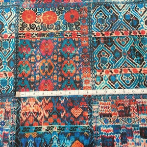 May include: A colorful fabric with a repeating pattern of geometric shapes in shades of blue, red, orange, and white. The fabric has a textured surface and a slightly faded look.