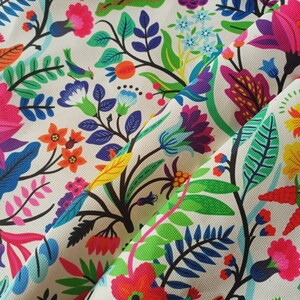 May include: A vibrant floral fabric featuring a repeating pattern of colorful flowers, leaves, and branches. The design includes pink, red, orange, blue, and green elements on a cream background. The fabric is folded, showing the texture and detail of the print.