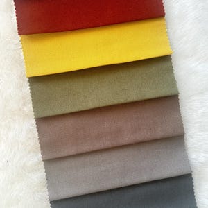 Puede incluir: Una colecci&oacute;n de ocho muestras de tela en diferentes colores, incluyendo gris, rojo, amarillo, verde, marr&oacute;n, beige, gris oscuro y negro. Las muestras est&aacute;n dispuestas en una pila vertical, con la muestra gris en la parte superior y la muestra negra en la parte inferior.
