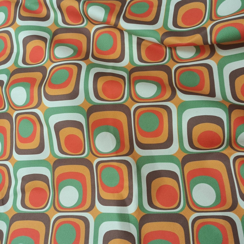 May include: A fabric with a repeating pattern of squares and circles in shades of brown, orange, green, and white.