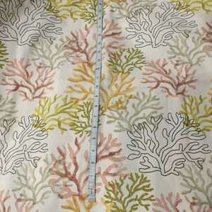 Puede incluir: Tela blanca con un patr&oacute;n repetitivo de ramas de coral en tonos de rosa, verde y amarillo. La tela se mide con una cinta m&eacute;trica.