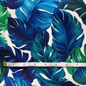 May include: Close-up of fabric with a tropical leaf pattern. The leaves are in shades of blue and green against a white background. A ruler shows the fabric is approximately 7 inches wide.