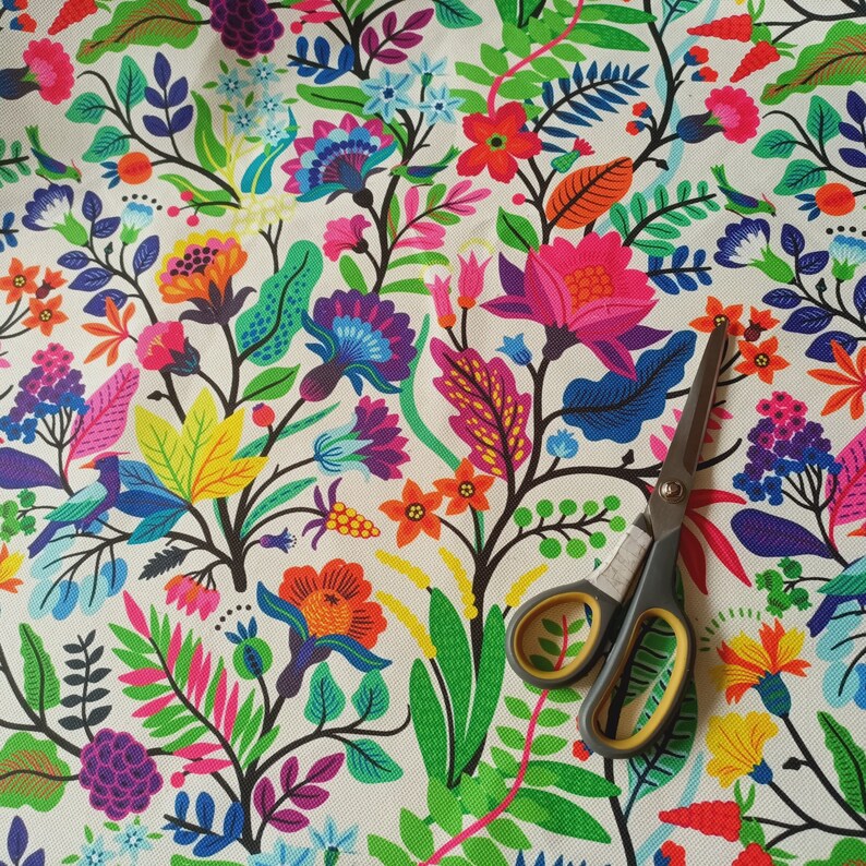 May include: Close-up of a vibrant floral fabric featuring a colorful array of flowers, leaves, and birds in shades of pink, orange, blue, and green. A pair of scissors with yellow handles rests on the fabric.