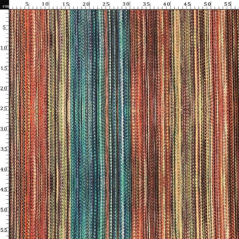 May include: A close-up of a textile with vertical stripes in various colors, including red, orange, yellow, green, and brown. The fabric appears to be woven with a textured surface. The image includes a centimeter ruler along the left side.