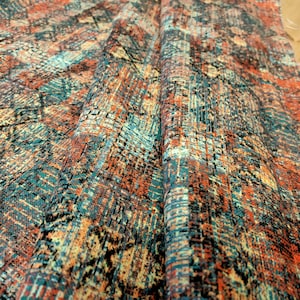 May include: Close-up of a fabric with a colorful abstract pattern in shades of orange, blue, and black. The fabric has a textured surface and a slightly faded look.