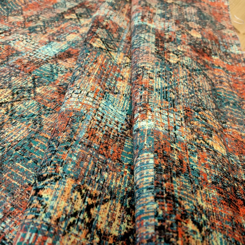 May include: Close-up of a fabric with a colorful abstract pattern in shades of orange, blue, and black. The fabric has a textured surface and a slightly faded look.