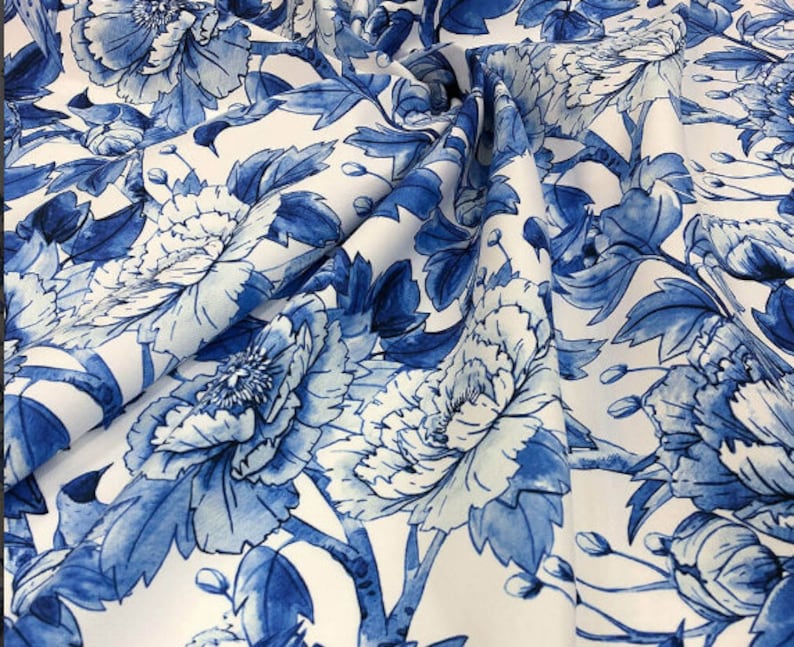 Op de afbeelding: Witte stof met een blauw bloemenpatroon. De bloemen zijn groot en hebben een aquareleffect. De stof is perfect voor knutselen, quilten of het maken van kleding.