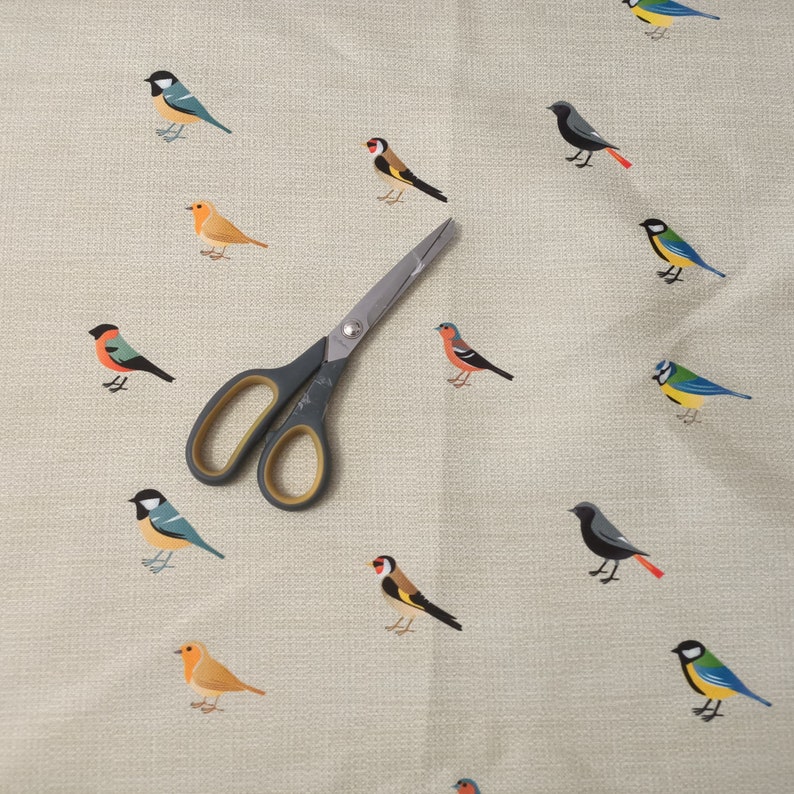 May include: A beige fabric with a repeating pattern of colorful birds. A pair of silver scissors is placed on the fabric.