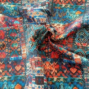 May include: A colorful fabric with a repeating geometric pattern in shades of blue, red, orange, and white. The fabric is folded and draped, showing the intricate details of the design.