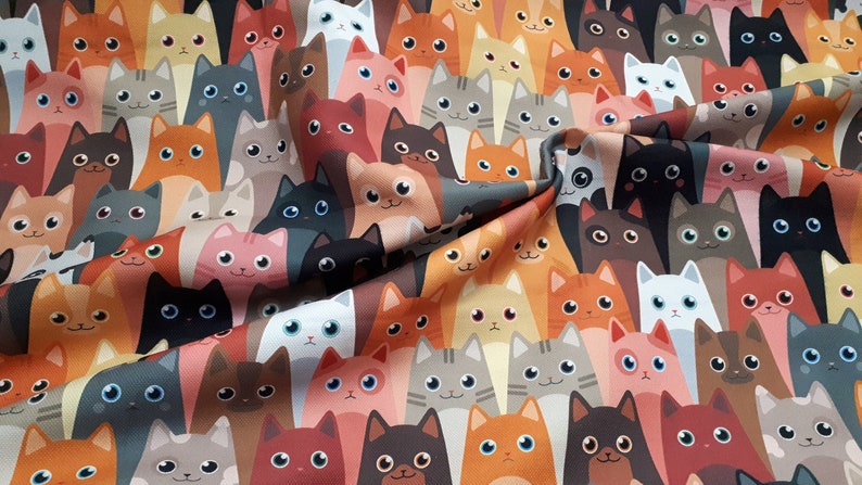 May include: A colorful fabric with a repeating pattern of cartoon cats in various colors and poses. The cats are all looking at the viewer with big eyes and smiling.