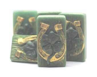 May include: A collection of green rectangular decorative tiles with gold-colored horseshoe and four-leaf clover designs. The tiles are arranged in a slightly overlapping pattern, showcasing the detailed relief work.