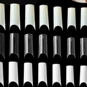 May include: A set of 24 clear and white plastic false nail tips in various sizes. The tips are curved and have a rounded edge. The tips are numbered 0-9.