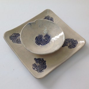 May include: A set of two ceramic dishes with a white glaze and blue floral designs. The smaller dish is nested inside the larger square dish.