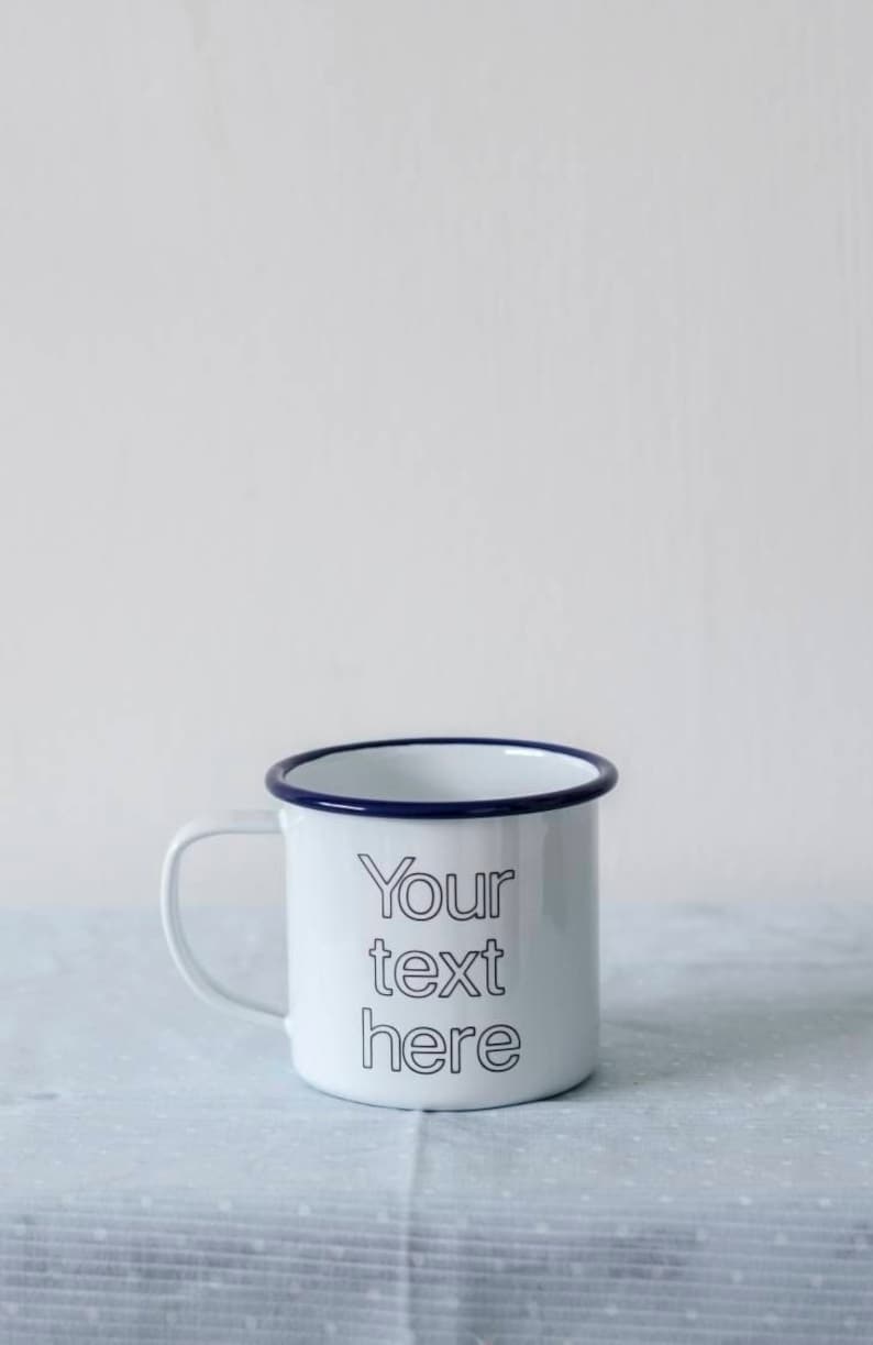 May include: White enamel mug with a blue rim and the text "Your text here" printed in black.