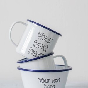 May include: Three white enamel mugs with blue rims stacked on top of each other. The top mug has the text "Your text here" printed on it. The bottom mug has the text "Your text here" printed on it.