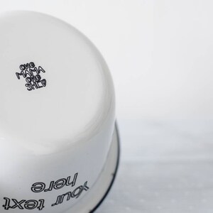 May include: White enamel bowl with black rim and text. The text on the bottom of the bowl reads "One Mama One Child". The text on the side of the bowl reads "Your text here".