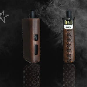 May include: Two brown leather vape devices with black accents are displayed against a dark background with a smoky effect. The device on the left has a rectangular shape, while the one on the right has a more elongated design with decorative stitching.