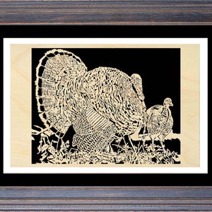 Puede incluir: Un recorte de madera en blanco y negro de un pavo con las plumas de la cola extendidas. Un pavo más pequeño está de pie detrás del más grande. El recorte está enmarcado en un marco de madera oscura.