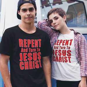 Op de afbeelding: Twee mensen dragen zwarte en witte T-shirts met de tekst "Repent And Turn To Jesus Christ" in rood. De persoon links draagt een zwart T-shirt en de persoon rechts draagt een wit T-shirt.