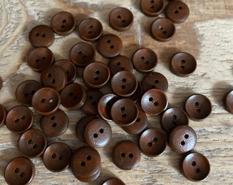 May include: A selection of small, round, dark brown wooden buttons, each with two holes. The buttons are arranged on a light brown, textured wooden surface. These buttons offer a natural, rustic look, perfect for sewing and craft activities.