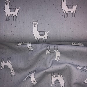 Könnte beinhalten: Hellgrauer Stoff mit einem sich wiederholenden Muster aus weißen Lamas mit grauen Satteldecken und kleinen schwarzen Punkten. Die Lamas sind in verschiedenen Posen, was ein verspieltes Design ergibt. Der Stoff ist wahrscheinlich Baumwolle oder ein ähnliches Material.