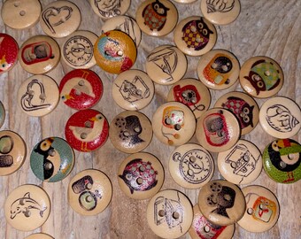 Puede incluir: Una colección de botones de madera con varios diseños, incluyendo búhos, peces y corazones. Los botones son de color marrón claro con ilustraciones negras y coloridas. Algunos botones tienen dos agujeros para coser.