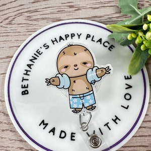 May include: White round badge holder with a purple border. The badge holder features a cartoon sloth wearing a blue life vest and blue and white patterned swim trunks. The text "Bethanie's Happy Place Made With Love" is printed around the sloth.