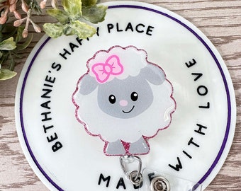 May include: White round badge with a purple border. The badge has a white fluffy sheep with a pink bow on its head. The text "Bethanie's Happy Place" is written around the sheep. The text "Made With Love" is written on the right side of the badge.