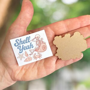 May include: A square sticker with the text "Shell Yeah" and a skeleton relaxing on a seashell, surrounded by starfish, shells, and a crab. A separate, blank, cloud-shaped sticker is also visible.