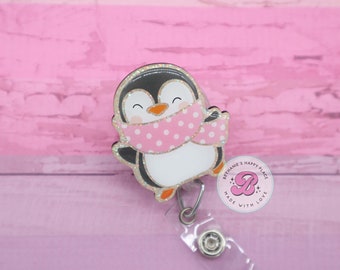 May include: A glitter penguin wearing a pink polka dot scarf with a retractable badge holder attached. The badge holder has a pink circle with the text "Bethanie's Happy Place" and a pink letter "B" with stars. The text "Made with Love" is written around the circle.