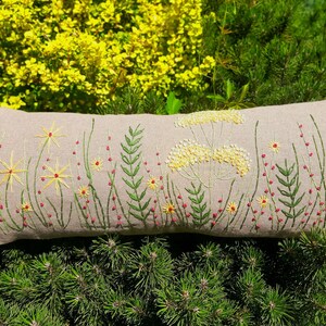 May include: A long, rectangular pillow with a beige linen fabric cover. The pillow is embroidered with a floral design featuring green stems, yellow flowers, and red berries.