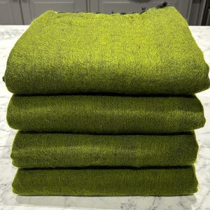 Op de afbeelding: Vier gevouwen groene dekens die op elkaar gestapeld zijn. De dekens zijn donkergroen en hebben een licht getextureerd oppervlak.