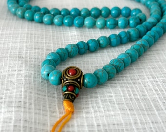 May include: A turquoise blue mala necklace with a decorative metal and red bead tassel. The necklace is made of round beads with a marbled pattern.
