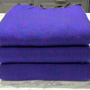 Op de afbeelding: Vier gevouwen paarse pashmina-sjaals, gestapeld op elkaar. De sjaals zijn gemaakt van zachte, luxe stof en hebben een subtiele glans.