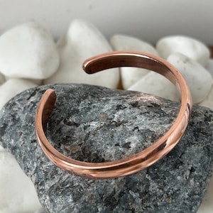 Peut inclure: Un bracelet en cuivre simple avec une finition lisse et polie. Le bracelet est ouvert aux deux extrémités et a une forme légèrement arrondie.