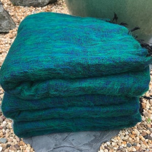 Könnte beinhalten: Ein gefalteter grüner und blauer Wollschal mit schwarzem Fransen. Der Schal ist aus weicher, flauschiger Wolle und perfekt, um sich an kalten Tagen warm zu halten.