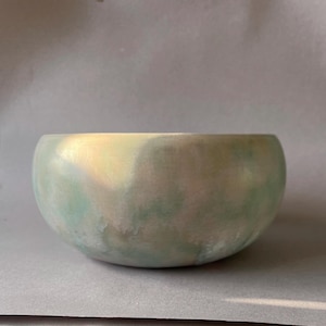 Op de afbeelding: Een ronde keramische kom met een gladde, matte afwerking. De kom heeft een mix van lichtgroene en crèmekleuren, met subtiele marmereffecten. Het ontwerp van de kom is eenvoudig en modern, geschikt voor diverse doeleinden.