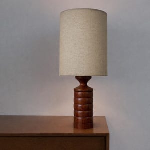 Puede incluir: Una taza de cerámica blanca con un asa negra y el texto "But First, Coffee" en negrita negra. La taza está sobre un fondo borroso. La taza mide aproximadamente 10 cm de altura.