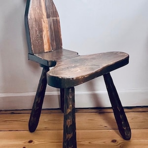 May include: A rustic wooden chair with a heart-shaped cutout in the back and three legs. The chair is made of dark brown wood with a natural wood grain.