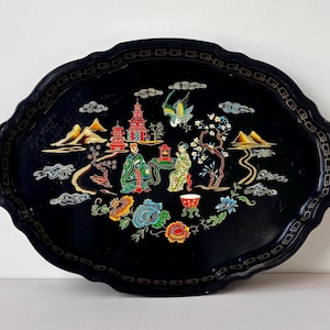 May include: Black oval serving tray with a scalloped edge. The tray features a colourful Asian-inspired design with pagodas, figures, flowers, and birds. The tray's border has a repeating geometric pattern.
