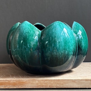 May include: A deep emerald green ceramic bowl with a glossy finish and a scalloped, petal-like rim. The bowl features a mottled, variegated glaze pattern that transitions from lighter teal tones to darker forest green shades across its surface.