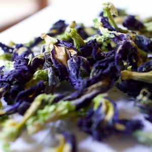 May include: Dried blue butterfly pea flowers, also known as blue tea, with green stems. The flowers are a vibrant blue color and have a delicate, papery texture.
