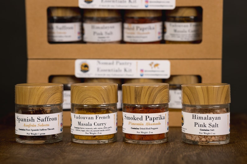 Op de afbeelding: Vier kleine glazen potjes met houten deksels die verschillende kruiden bevatten. De potjes zijn gelabeld met "Spaanse Saffraan", "Vadouvan Franse Masala Curry", "Gerookte Paprika" en "Himalaya roze zout".