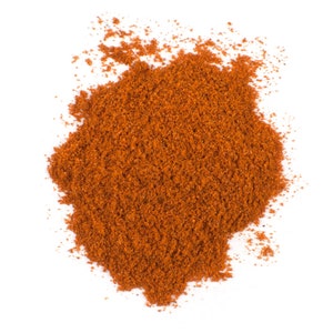 Puede incluir: Un mont&oacute;n de especias de color marr&oacute;n rojizo finamente molidas, probablemente piment&oacute;n o chile en polvo, sobre un fondo blanco limpio. La textura parece granular y ligeramente &aacute;spera, lo que sugiere una mezcla de ingredientes secos.