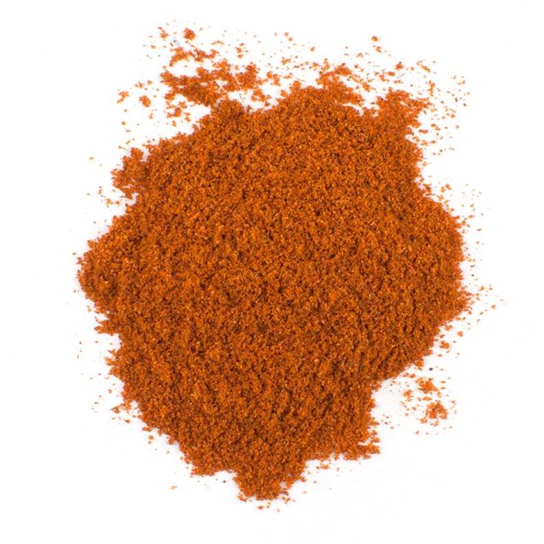 Puede incluir: Un mont&oacute;n de especias de color marr&oacute;n rojizo finamente molidas, probablemente piment&oacute;n o chile en polvo, sobre un fondo blanco limpio. La textura parece granular y ligeramente &aacute;spera, lo que sugiere una mezcla de ingredientes secos.